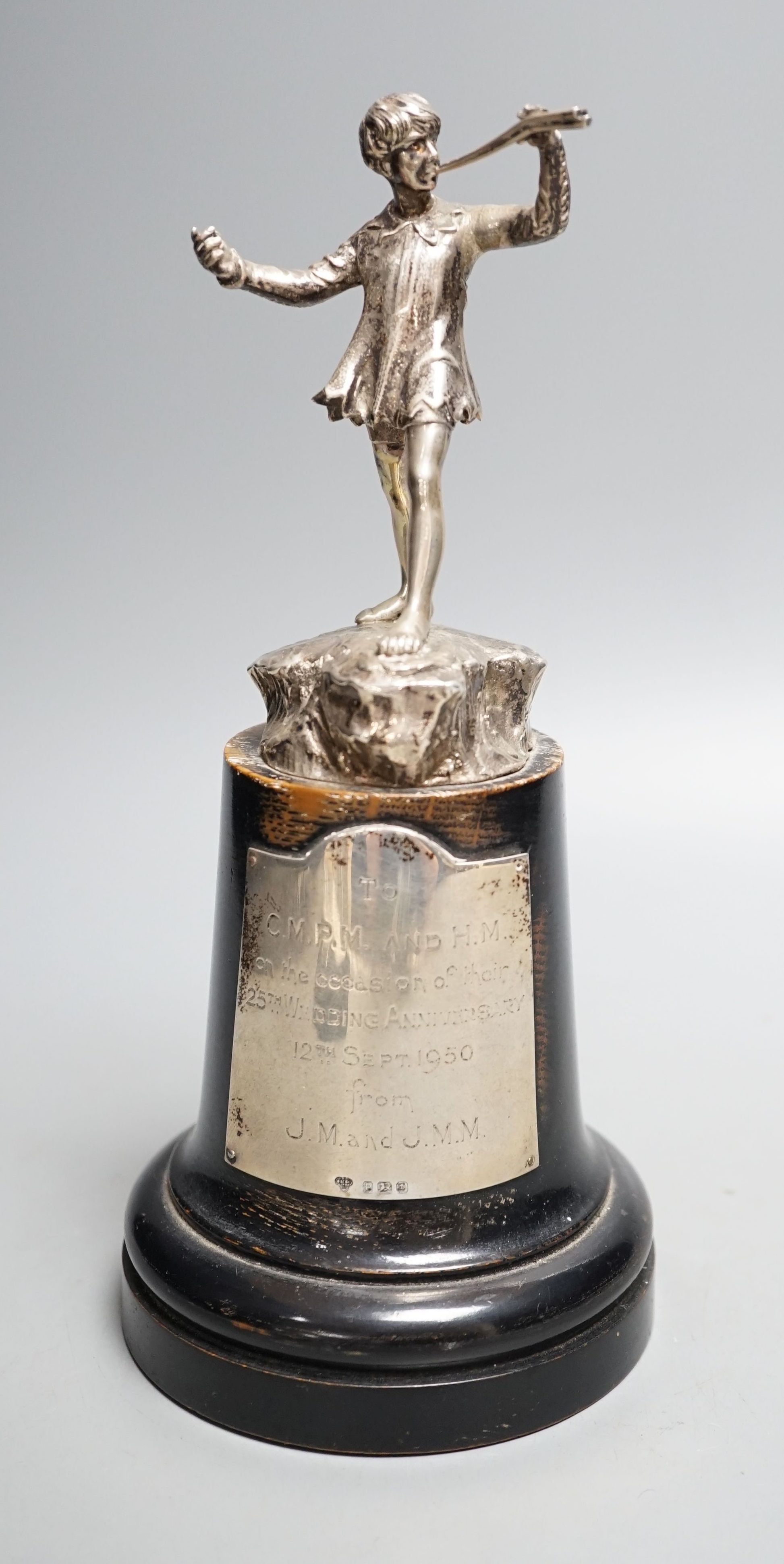 A late 1940's silver presentation figure of a young boy playing the pipes, on a rocky base, Goldsmiths & Silversmiths Co Ltd, London, 1949, on a wooden plinth with engraved presentation plaque, overall height 23.5cm